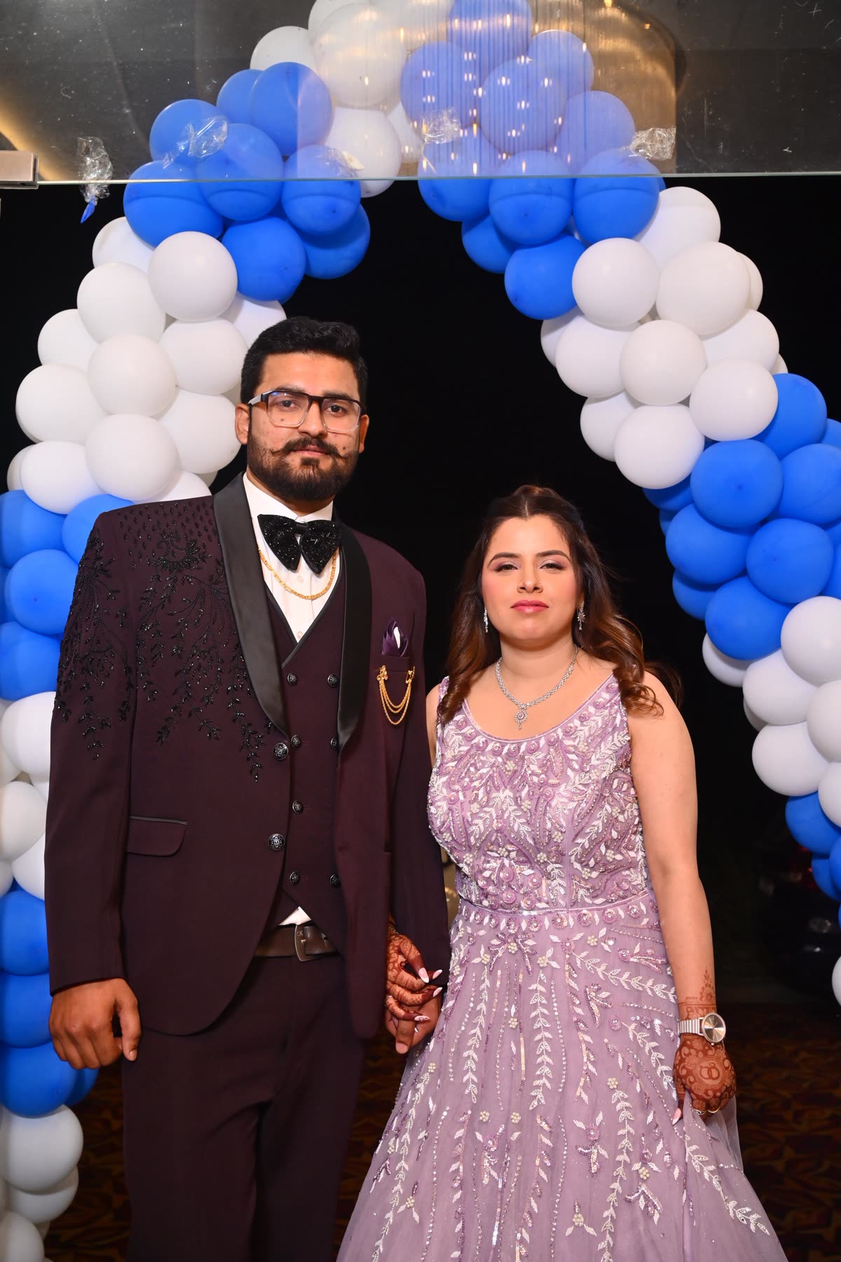 Anukriti and Anmol posing in front of a blue and white balloon arch